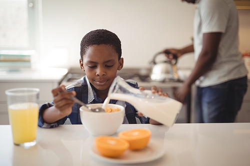 Boy pouring milk into breakfast cereals bowl in kitchen at home