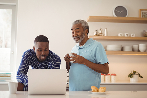 Smiling father and son using laptop while having coffee in kitchen