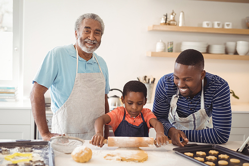 Boy preparing cookie dough with his father and grandfather in kitchen at home