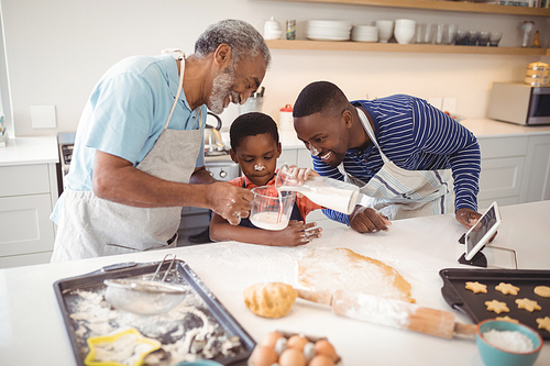 Multi-generation pouring milk in a jar while preparing cookies in the kitchen