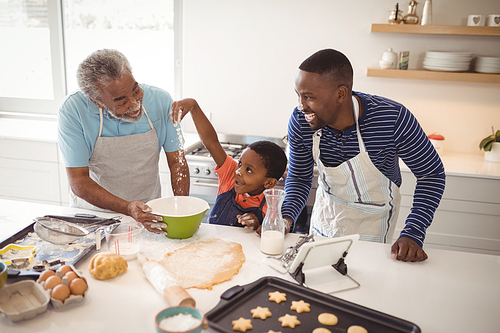 Boy playing with the flour while preparing cookies with his father and grandfather