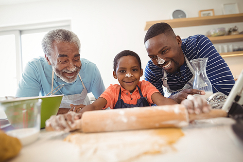 Boy preparing cookie dough with his father and grandfather in kitchen at home