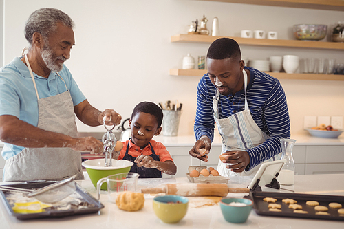 Boy learning to whisk the eggs while preparing cookies with his father and grandfather