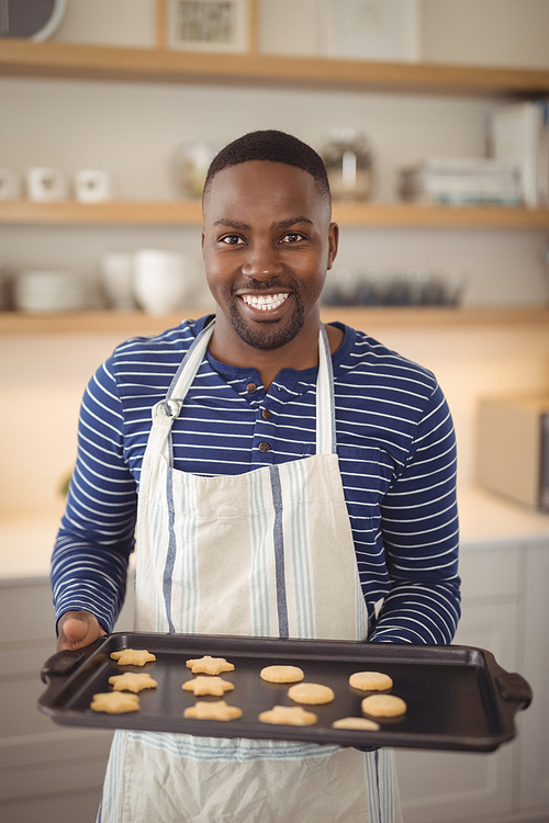 Portrait of smiling man holding tray of cookies in kitchen at home