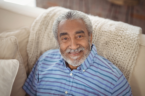 Portrait of smiling senior man sitting on sofa in living room at home