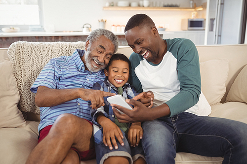 Smiling multi-generation family using mobile phone in living room at home