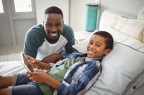 Portrait of smiling father and son with digital tablet in bedroom