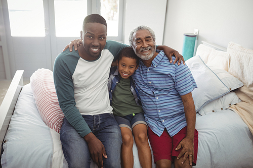 Portrait of smiling multi-generation family sitting together on bed in bedroom