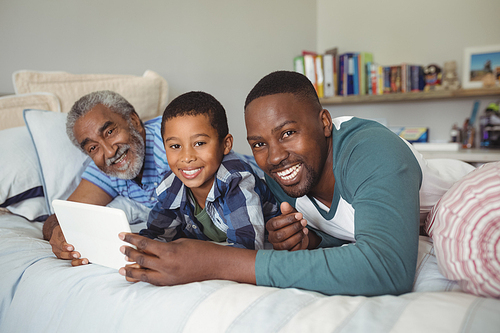 Portrait of happy multi-generation family using digital tablet on bed in bedroom