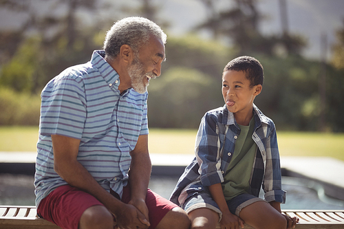 Grandson and grandfather making funny faces near poolside on a sunny day