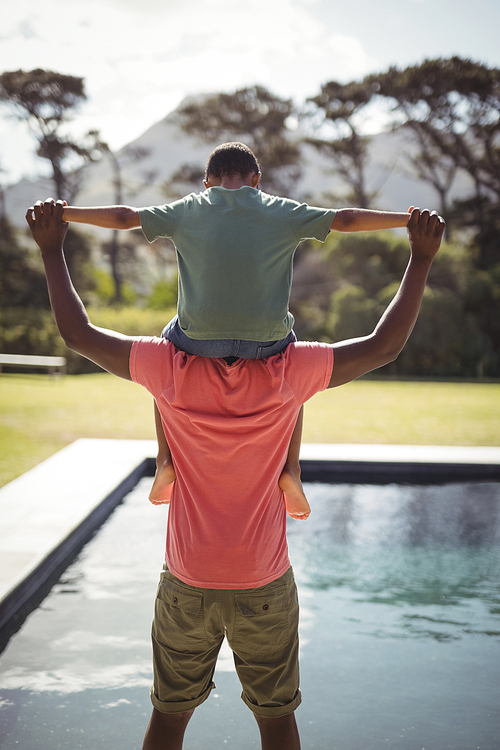 Rear view of father carrying son on shoulders near poolside