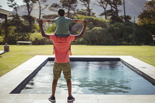 Rear view of father carrying son on shoulders near poolside