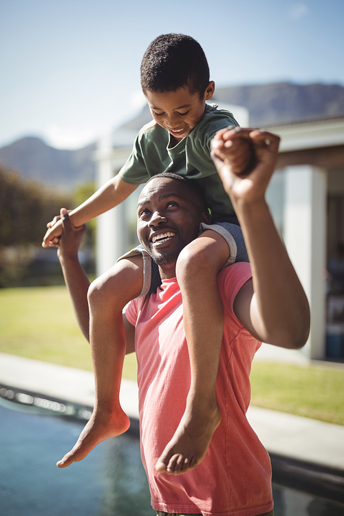 Happy father carrying son on shoulders near poolside