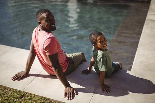Portrait of smiling father and son sitting on edge of swimming pool