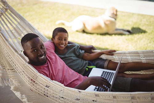 Happy father and son using laptop while relaxing on a hammock