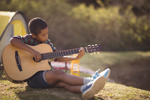 Portrait of smiling boy playing guitar in park on a sunny day