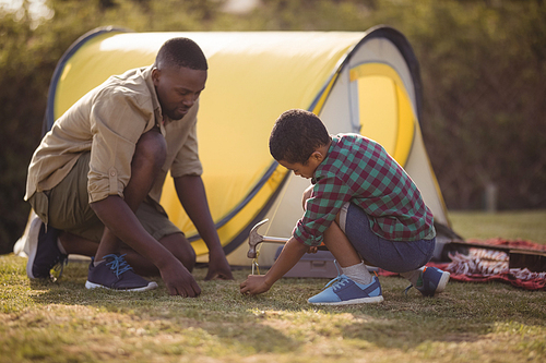 Father and son pitching their tent in park on a sunny day