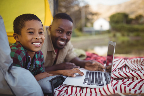 Portrait of smiling father and son using laptop in tent