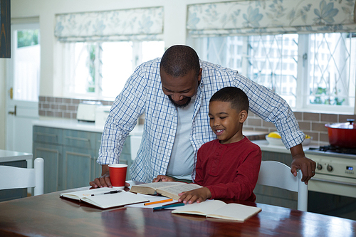 Father helping his son with homework in kitchen at home