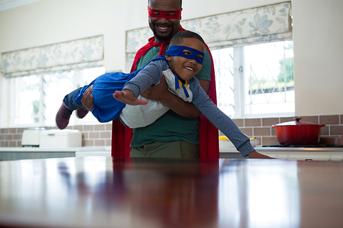 Son and father pretending to be a superhero in kitchen at home