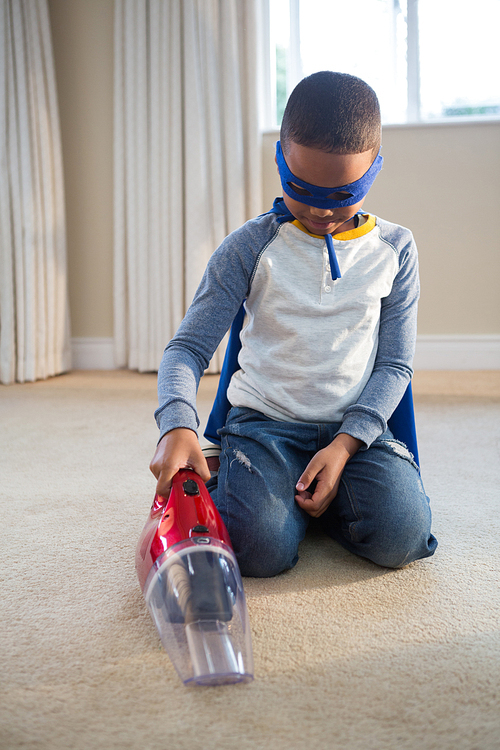 Boy in superhero costume cleaning a floor with vacuum cleaner at home