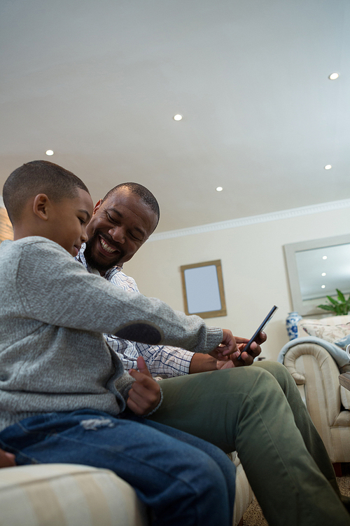 Father and son using mobile phone on sofa in living room at home