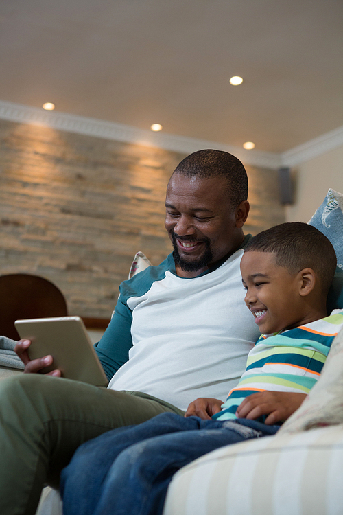 Smiling father and son using digital tablet on sofa in living room