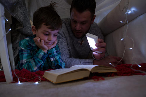 Father and son reading book under shelter in bedroom