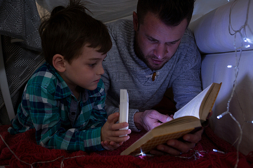 Father and son reading book under shelter in bedroom