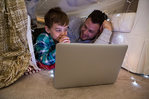 Father and son using laptop in bedroom