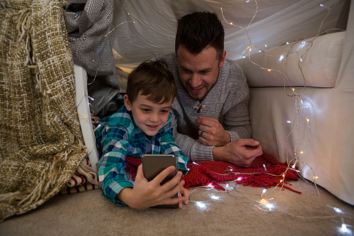 Father and son using mobile phone in bedroom