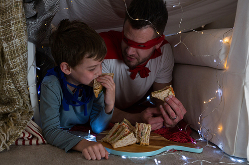 Father and son pretending to be superhero while eating sandwich