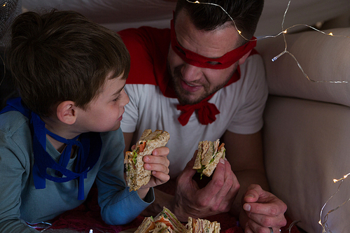 Father and son pretending to be superhero while eating sandwich