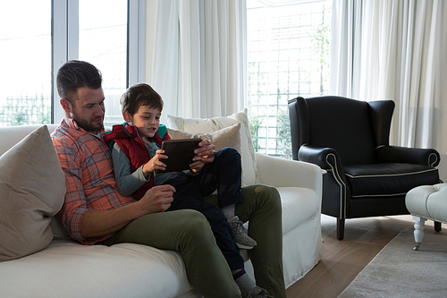 Father and son using digital tablet in living room at home