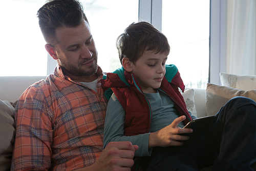 Father and son using digital tablet in living room at home