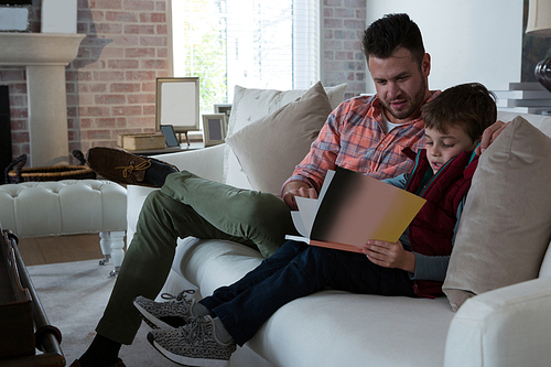 Father ans son reading book in living room at home