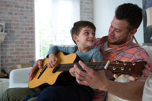 Father assisting his son in playing guitar in living room