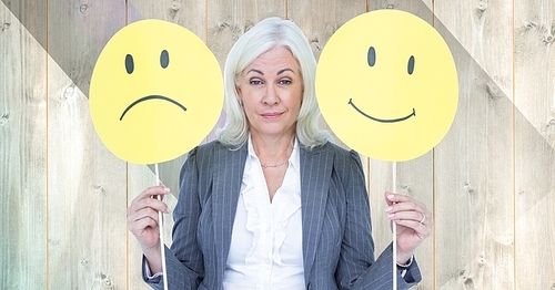 Digital composition of senior businesswoman holding smiley faces against wooden background