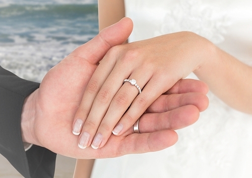 Close-up of newly wed couple holding hands on beach