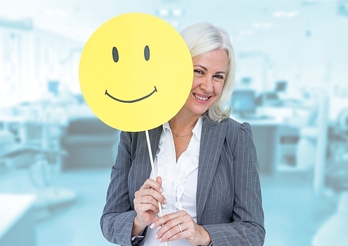Digital composition of senior businesswoman holding smiley face against wooden background