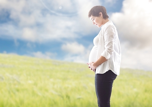 Smiling pregnant woman touching around the abdomen against greenery background