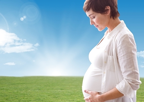 Digital composite image of pregnant woman looking a her belly against landscape