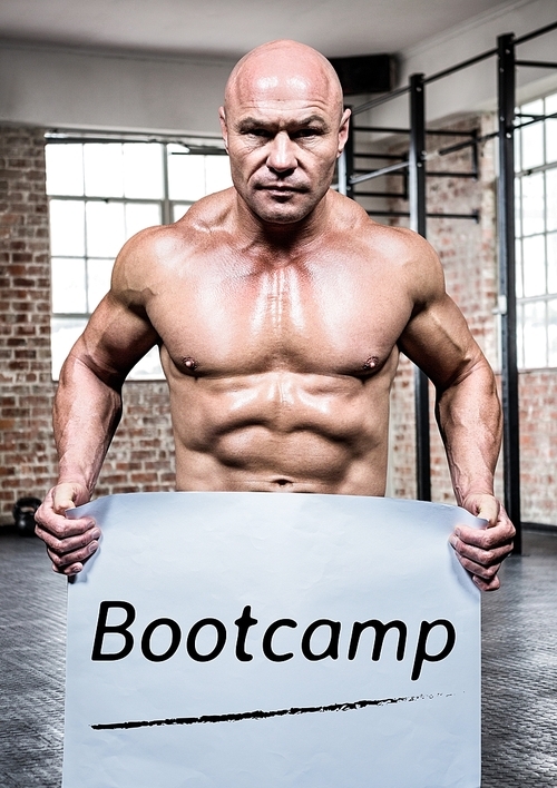 Portrait of bodybuilder holding placard with text bootcamp in gym