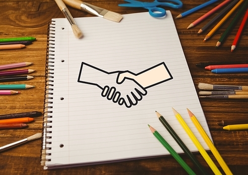 Digital composition of drawn handshake shape on notebook with color pencils on wooden table