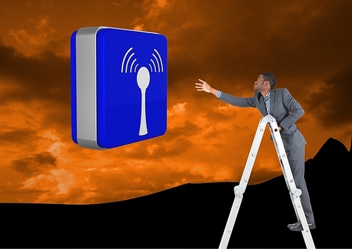Digital composite of Businessman on a Ladder trying to hold a blue icon against an orange mountain background