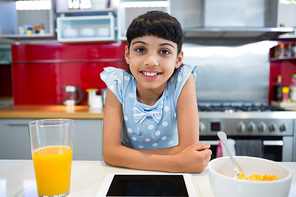 Portrait of smiling girl sitting with tablet and breakfast in kitchen at home