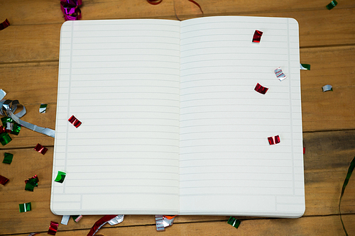 Overhead of open note book with confetti on wooden surface