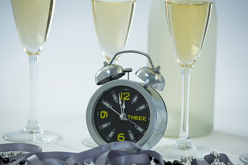 Close-up of champagne with alarm clock and glass on white background