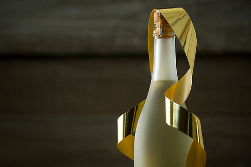 Close-up of champagne bottle with golden ribbon against wooden background