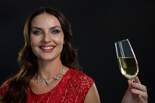 Portrait of smiling woman holding glass of champagne against black background